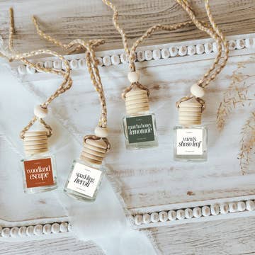 Four decorative fragrance bottles with wooden caps, arranged on a textured surface with a white ribbon and natural elements.